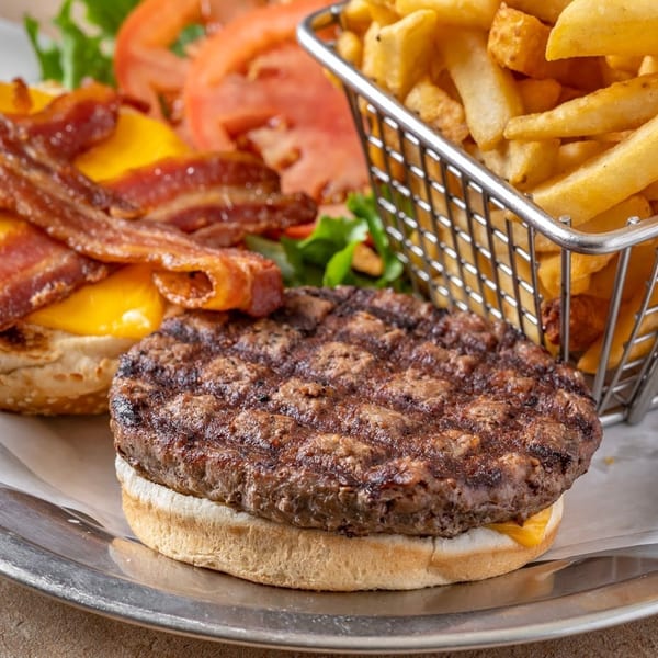 Deconstructed bacon cheeseburger with a side of golden french fries in a metal basket.