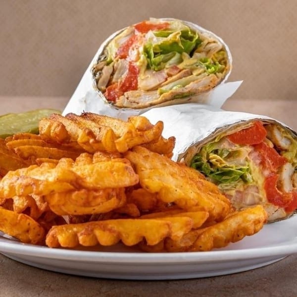 Two chicken wraps with lettuce and tomato, waffle fries, and a pickle spear on a white plate.